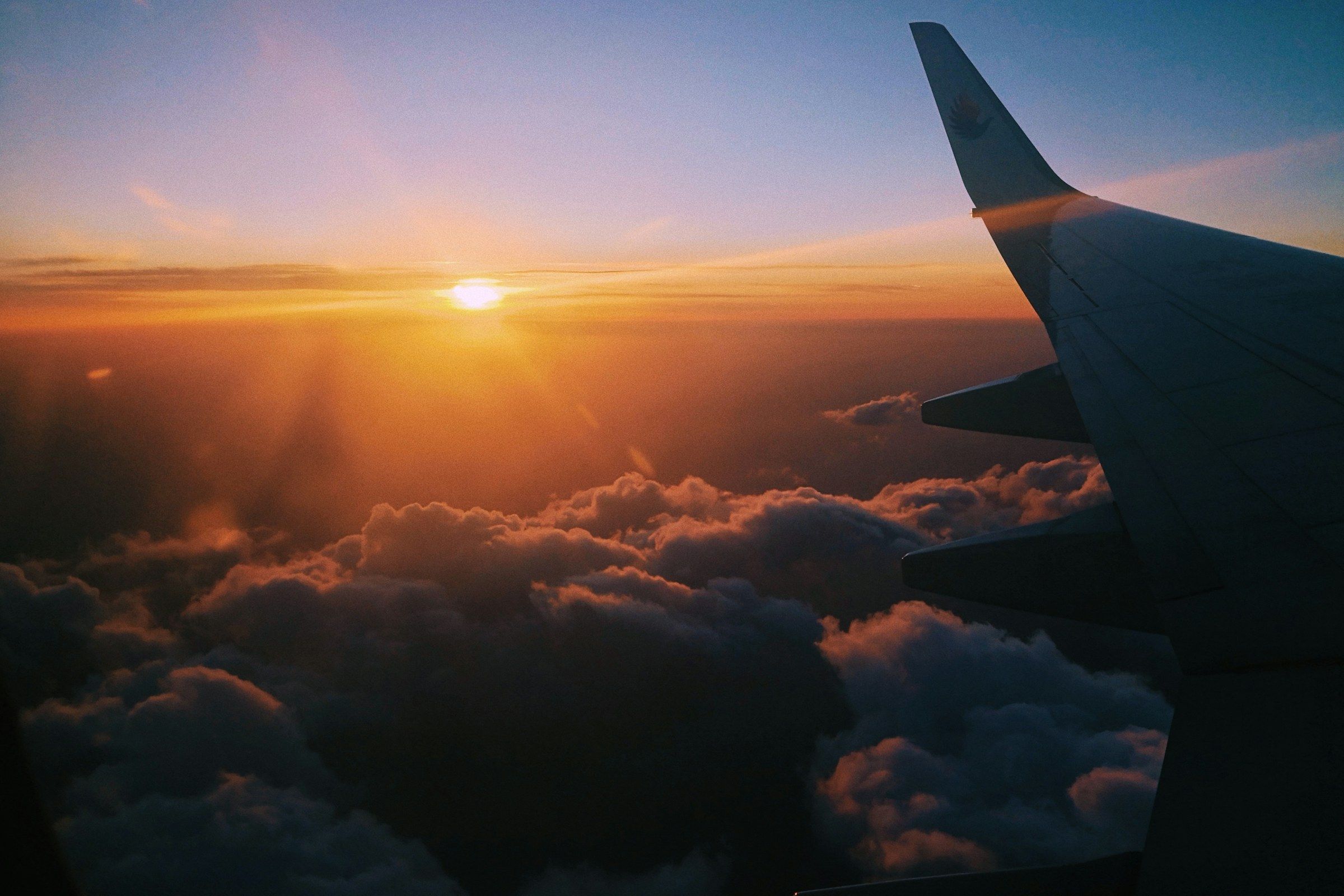 Asa de avião sobre um mar de nuvens no pôr do sol